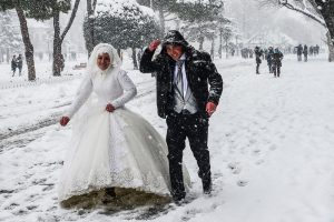 A newly married couple walk at Sultanahmet square during snowfalls in Istanbul on January 8, 2017. / AFP PHOTO / YASIN AKGUL
