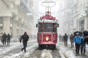 People walk next to a tramway on İstiklal avenue during snowfalls in Istanbul on January 7, 2017. A heavy snowstorm paralysed life in Istanbul with hundreds of flights cancelled and the Bosphorus closed to shipping traffic. The snowstorm dumped almost 40 centimetres (16 inches) of snow in parts of the Turkish metropolis overnight, causing havoc on roads as travellers sought to leave the city for the weekend getaway. / AFP PHOTO / YASIN AKGUL